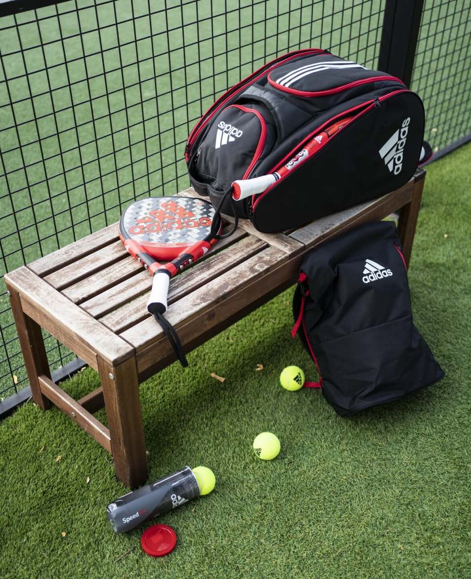 Adidas Metalbone 3.1 2022 och tillbehör. Bild som visar padelracket Adidas Metalbone 2022 liggandes vid padelbanan tillsammans med en Adidas padelväska och Adidas padelbollar.