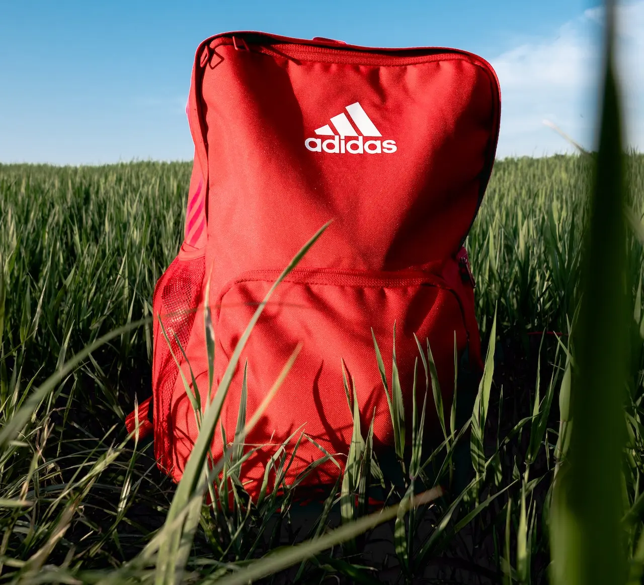 En röd padelryggsäck av märket Adidas som står på en äng.