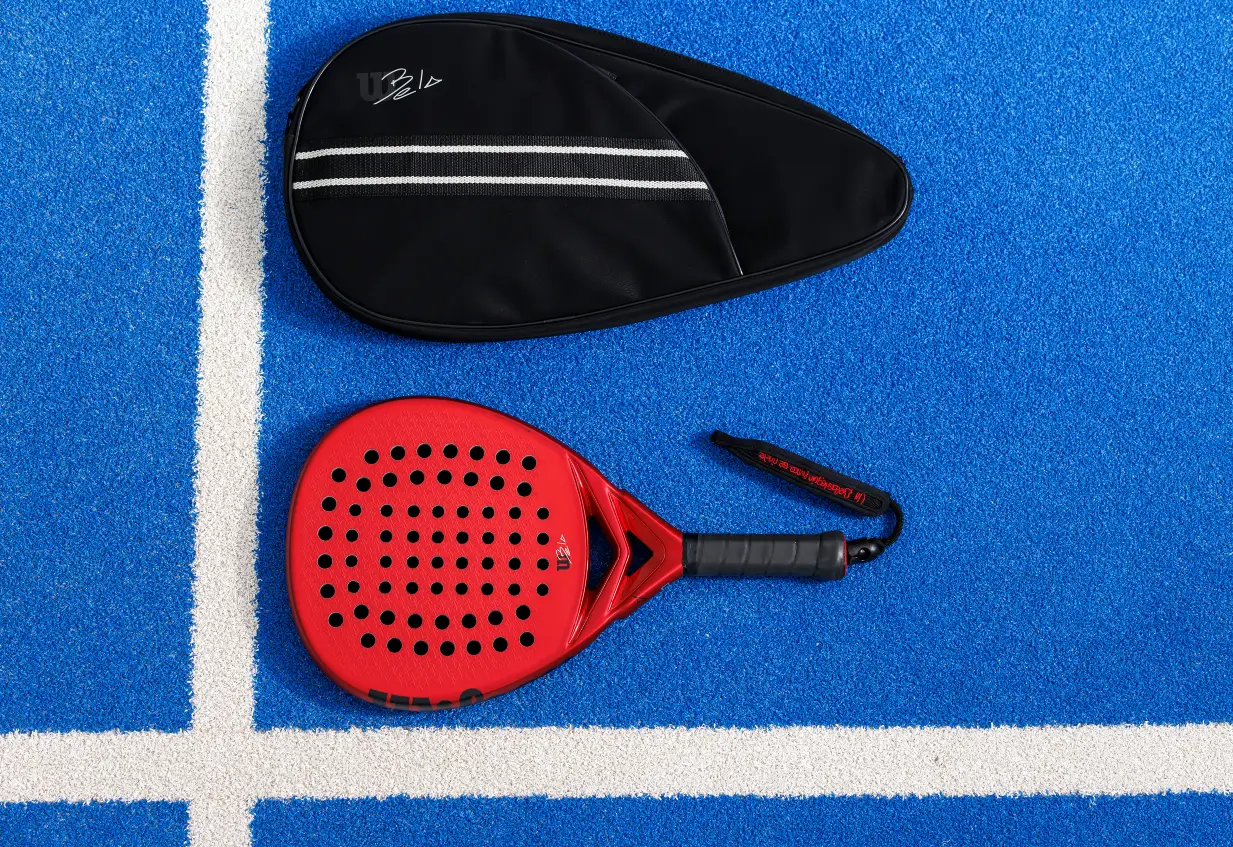 Wilson Bela Pro V2 2023 test, betyg, omdöme. Här ser man racket liggandes på padelbanan tillsammans med ett fodral.